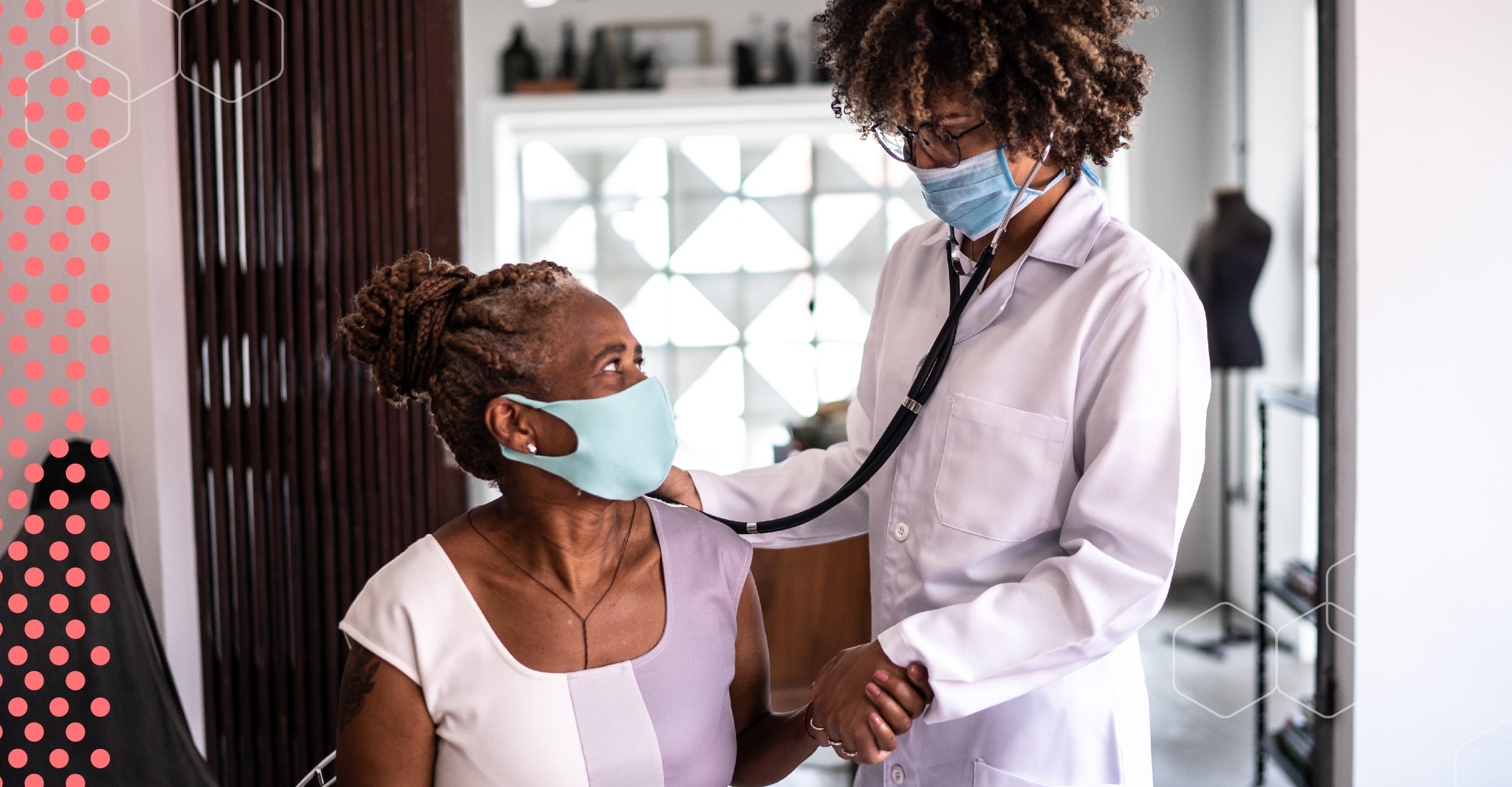 Two Black women, a doctor and a patient, hold hands during a check-up.