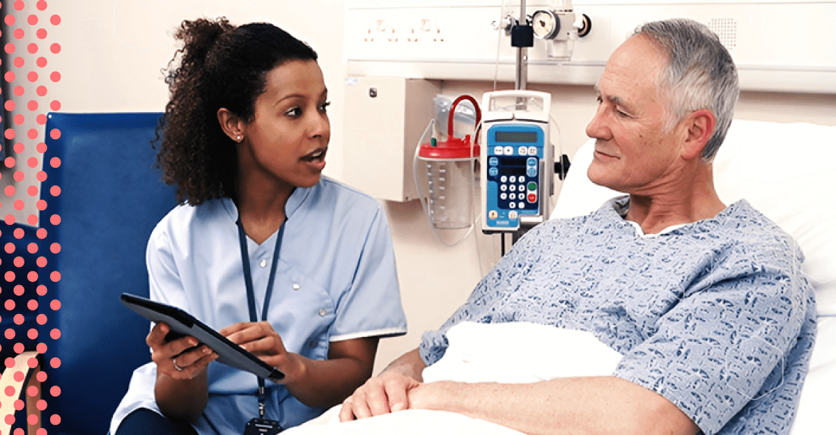 A doctor speaks with and sits next to a man in a hospital bed.